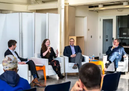 four people sit in chairs speaking to a crowd