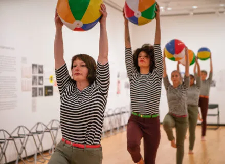 several people wearing striped shirts hold up colorful beach balls 